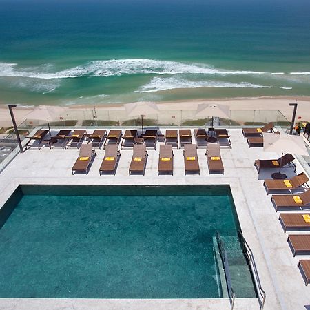 Windsor Marapendi Hotel Rio de Janeiro Luaran gambar The photo shows a rooftop area with a swimming pool and several lounge chairs arranged around it. The pool has a clear blue surface, and the lounge chairs are positioned in a neat row, some with yellow cushions. In the background, you can see a beaut