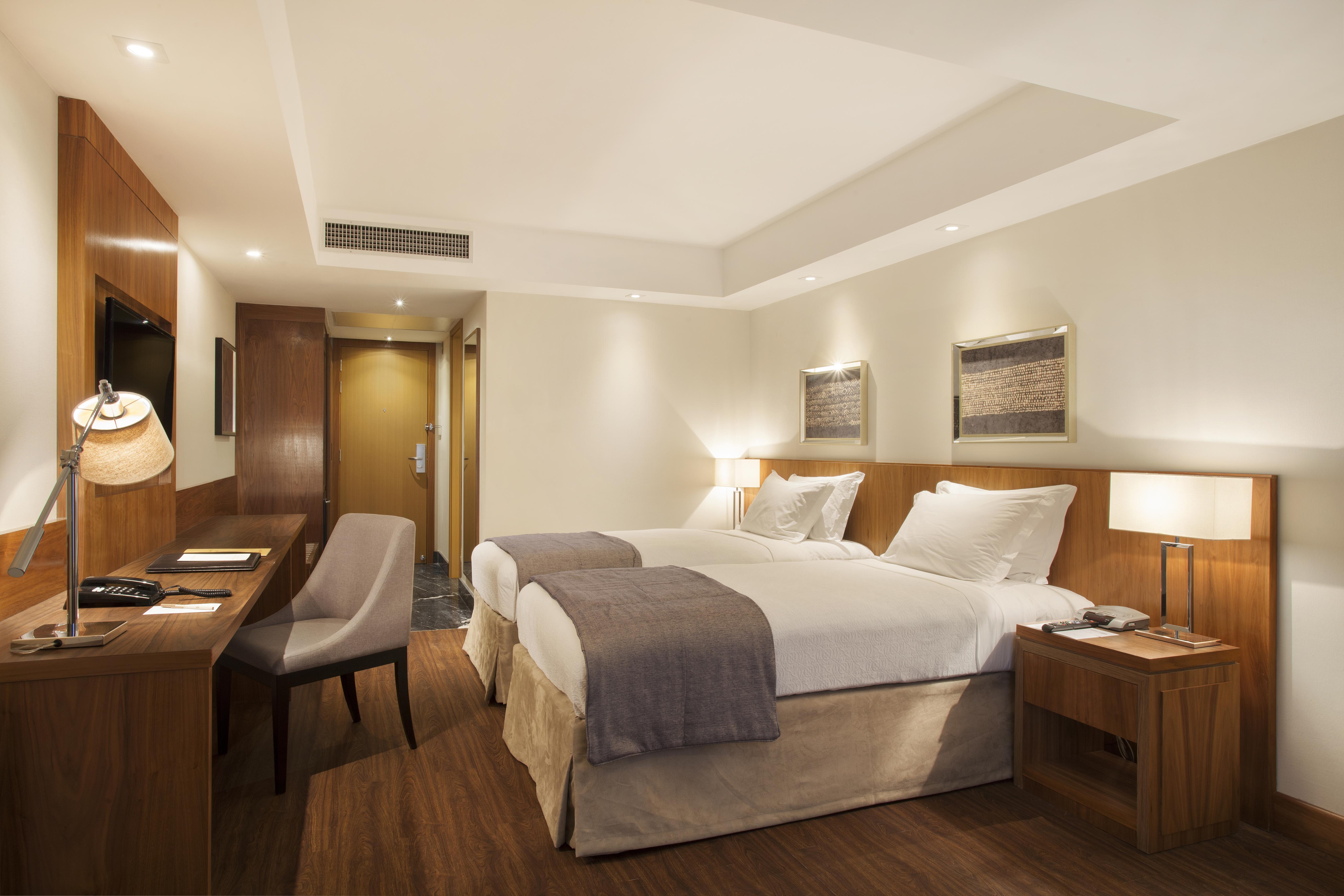 Windsor Marapendi Hotel Rio de Janeiro Luaran gambar The photo displays a modern hotel room featuring two twin beds with crisp white linens and gray throw blankets. The room has a clean and minimalist design, with wooden accents, including a bedside table and a desk. To the left, there's a small desk a