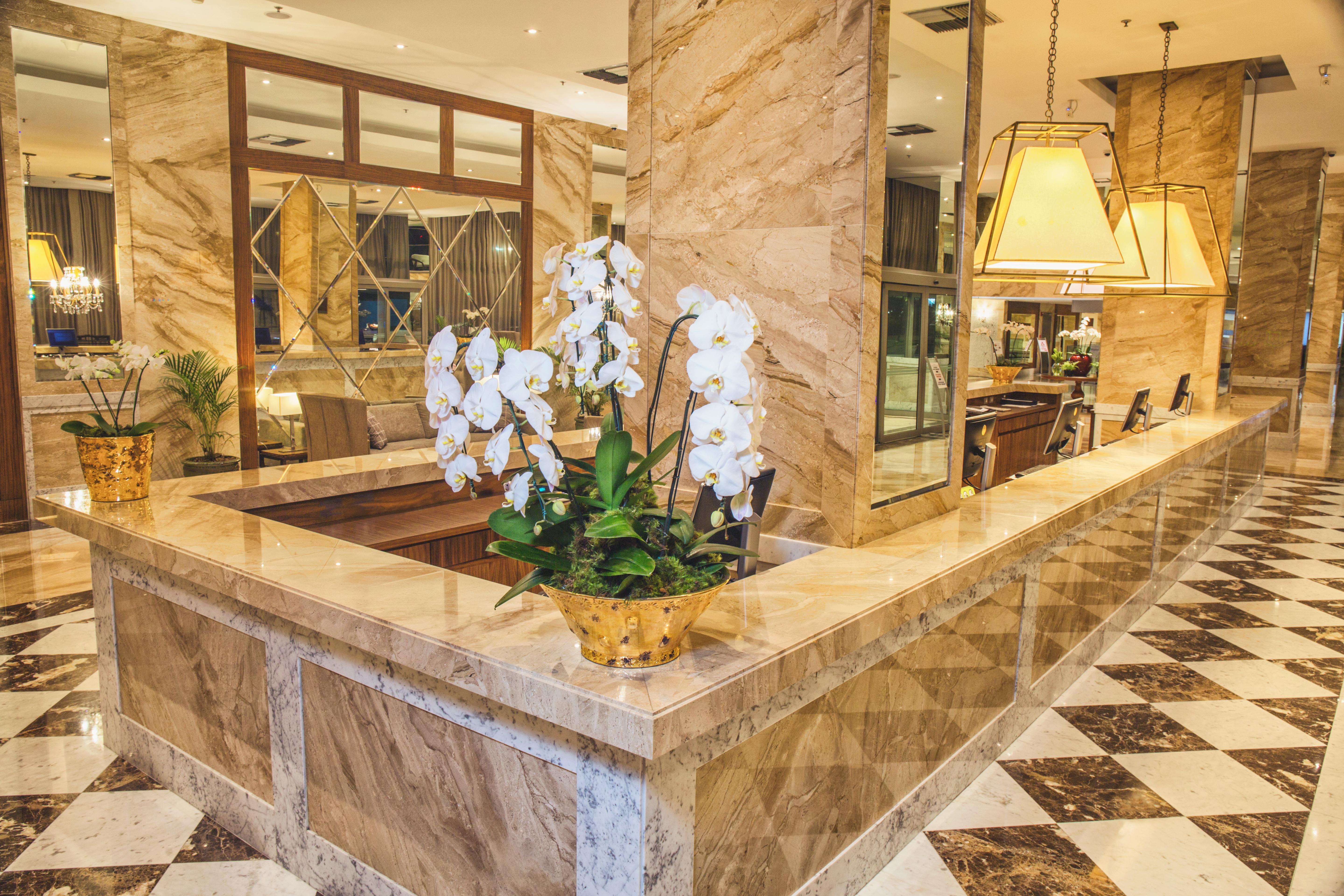 Windsor Marapendi Hotel Rio de Janeiro Luaran gambar The photo depicts a luxurious hotel lobby featuring a polished marble reception desk. There are elegant white orchids arranged in a gold pot on the counter, adding a touch of sophistication. The surrounding interior showcases marble walls, stylish li