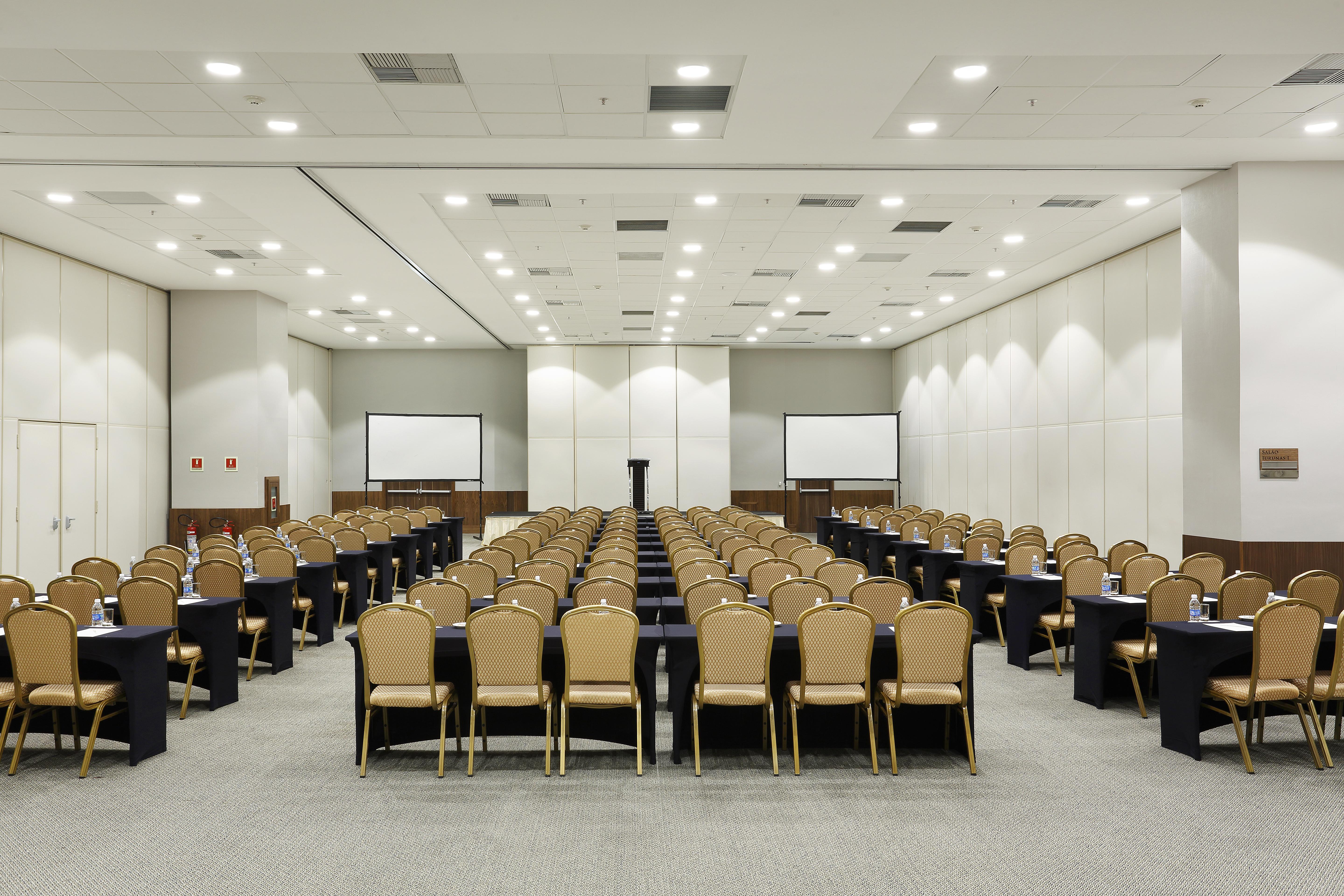 Windsor Marapendi Hotel Rio de Janeiro Luaran gambar The photo shows a conference room arranged for an event or meeting. There are rows of neatly arranged chairs with golden frames, paired with black tables. The room has bright overhead lighting and features two blank screens in the front, likely for p