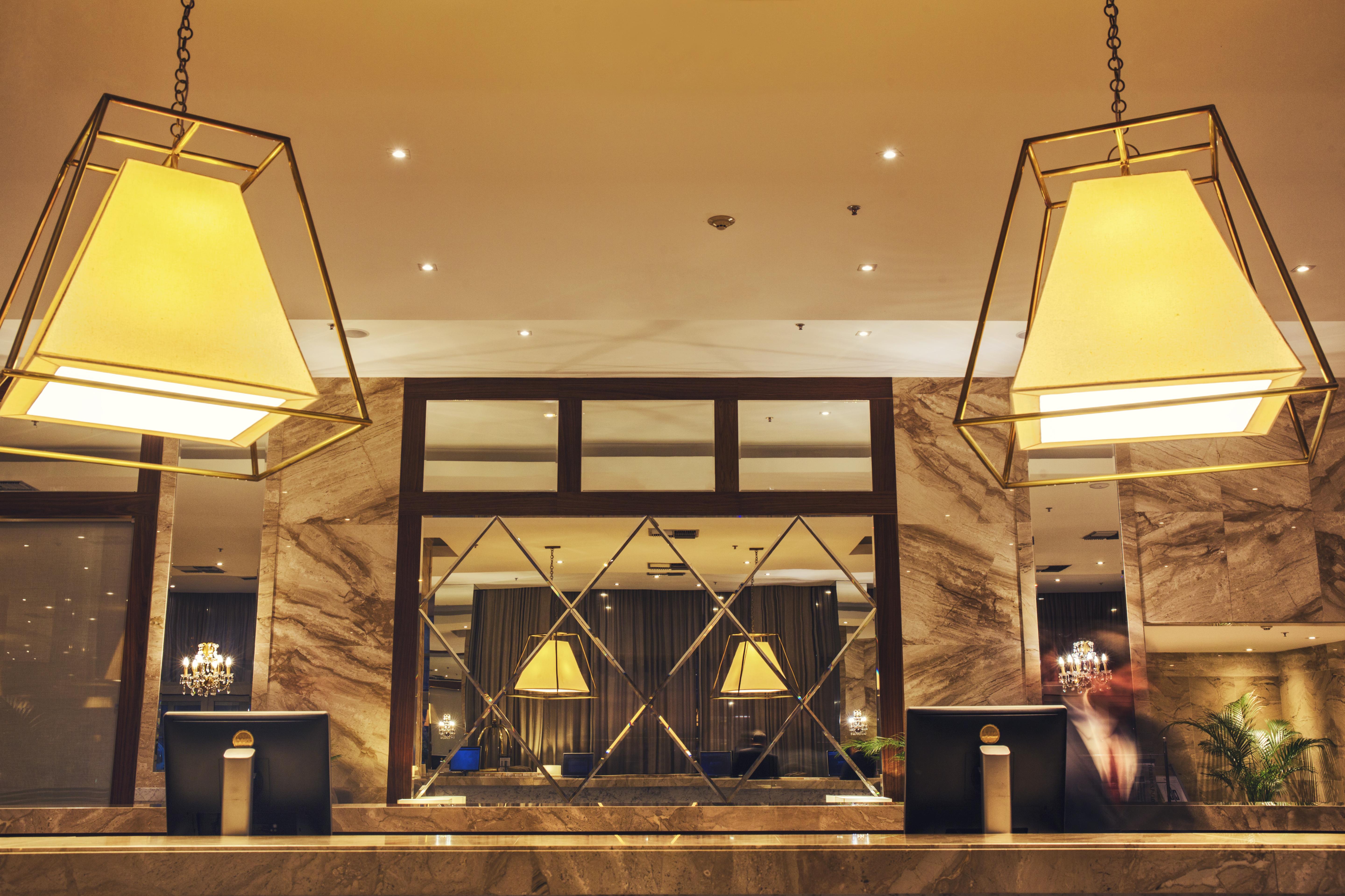 Windsor Marapendi Hotel Rio de Janeiro Luaran gambar The photo shows a hotel lobby or reception area. There are large geometric light fixtures hanging from the ceiling, providing a warm glow to the space. The reception desk is made of a polished material, likely marble, with decorative elements and two
